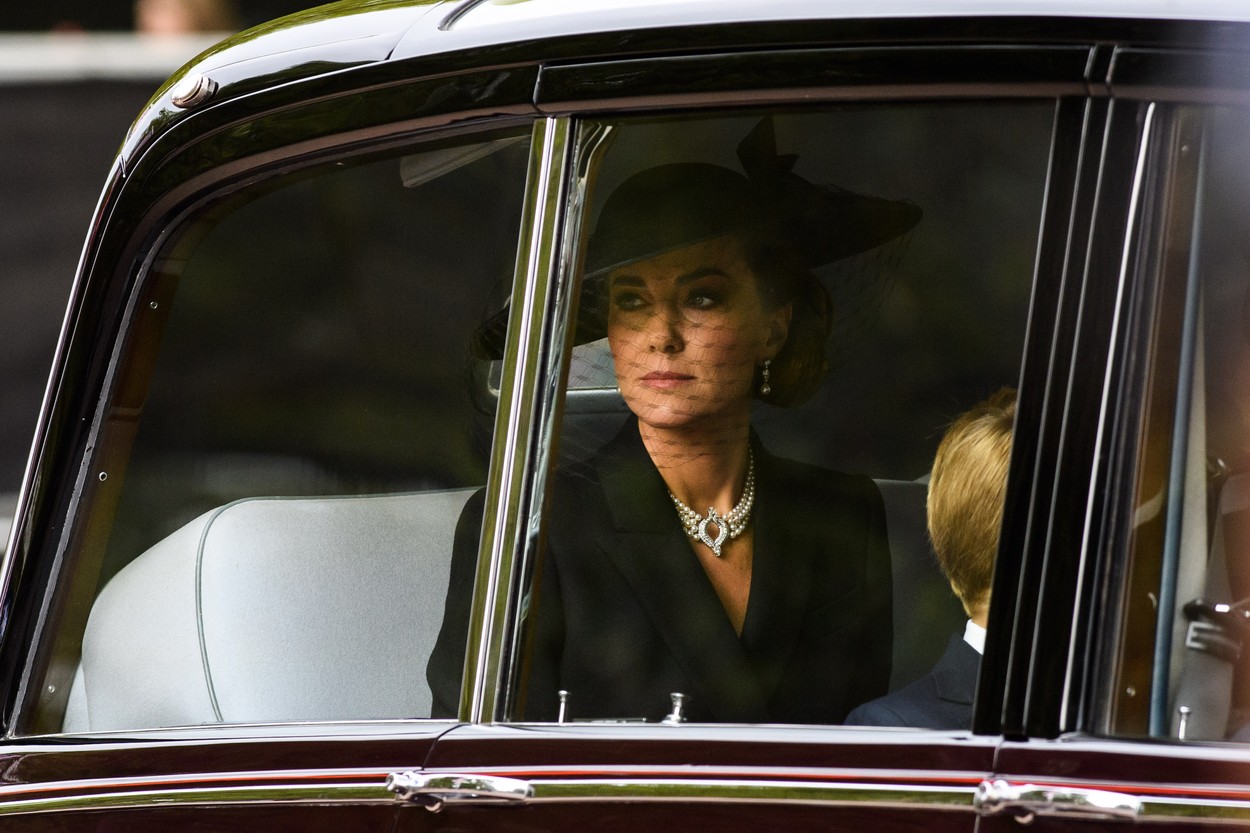 За тъжното събитие Катрин, принцесата на Уелс, комбинира любимите перли на кралицата с палтото на Alexander McQueen, а шапката – тя просто е задължителен аксесоар за специалните поводи.